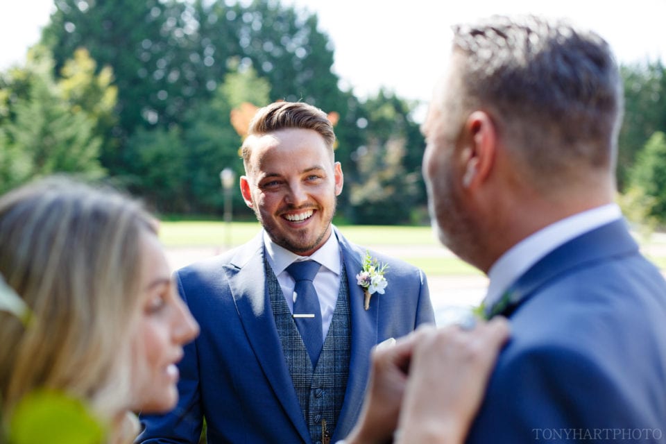 Groom Tom looks on as Hannah Berry Flowers attaches the Best Man's buttonhole